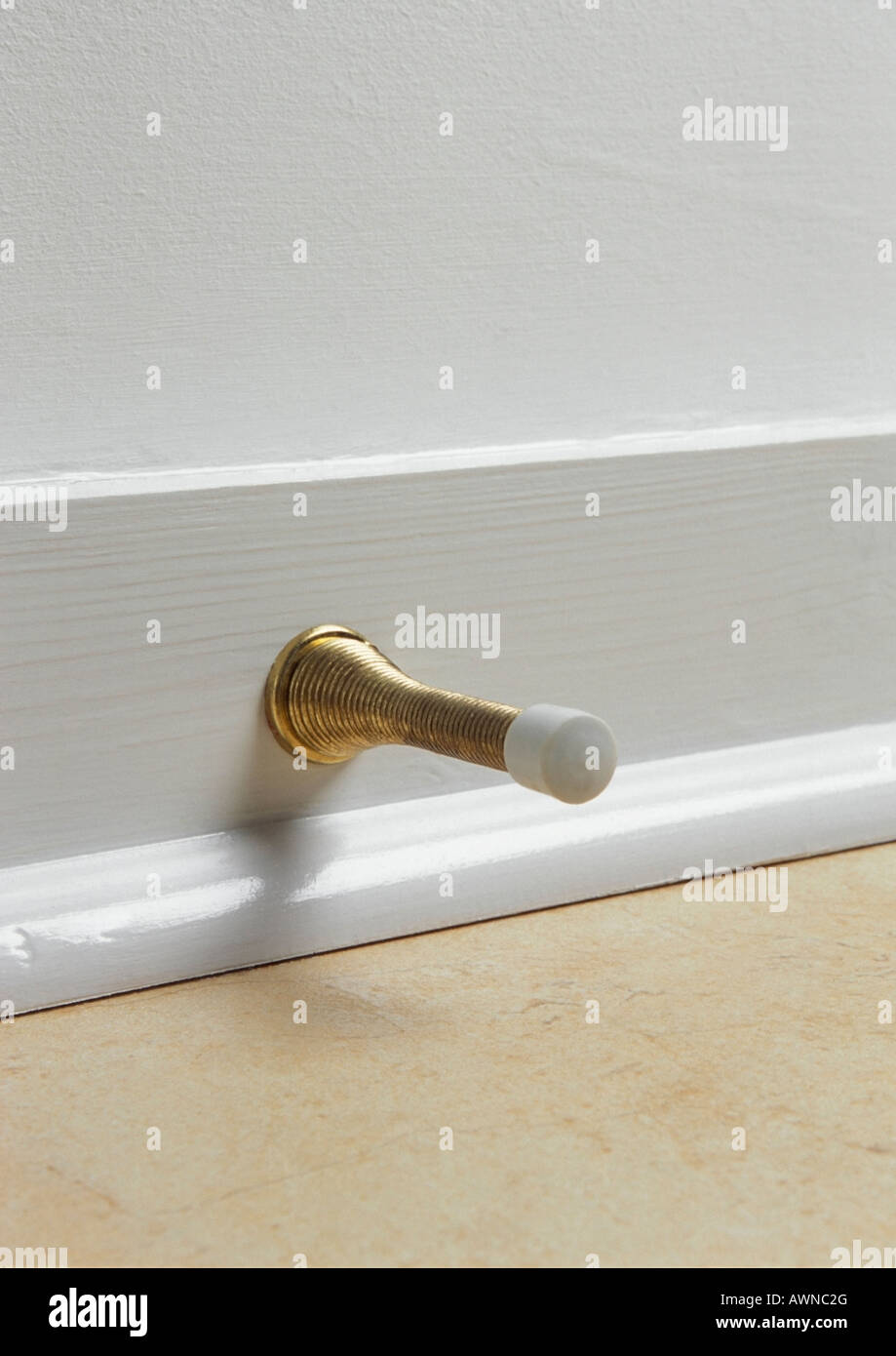 Brass spring door stop on white skirting board Stock Photo Alamy