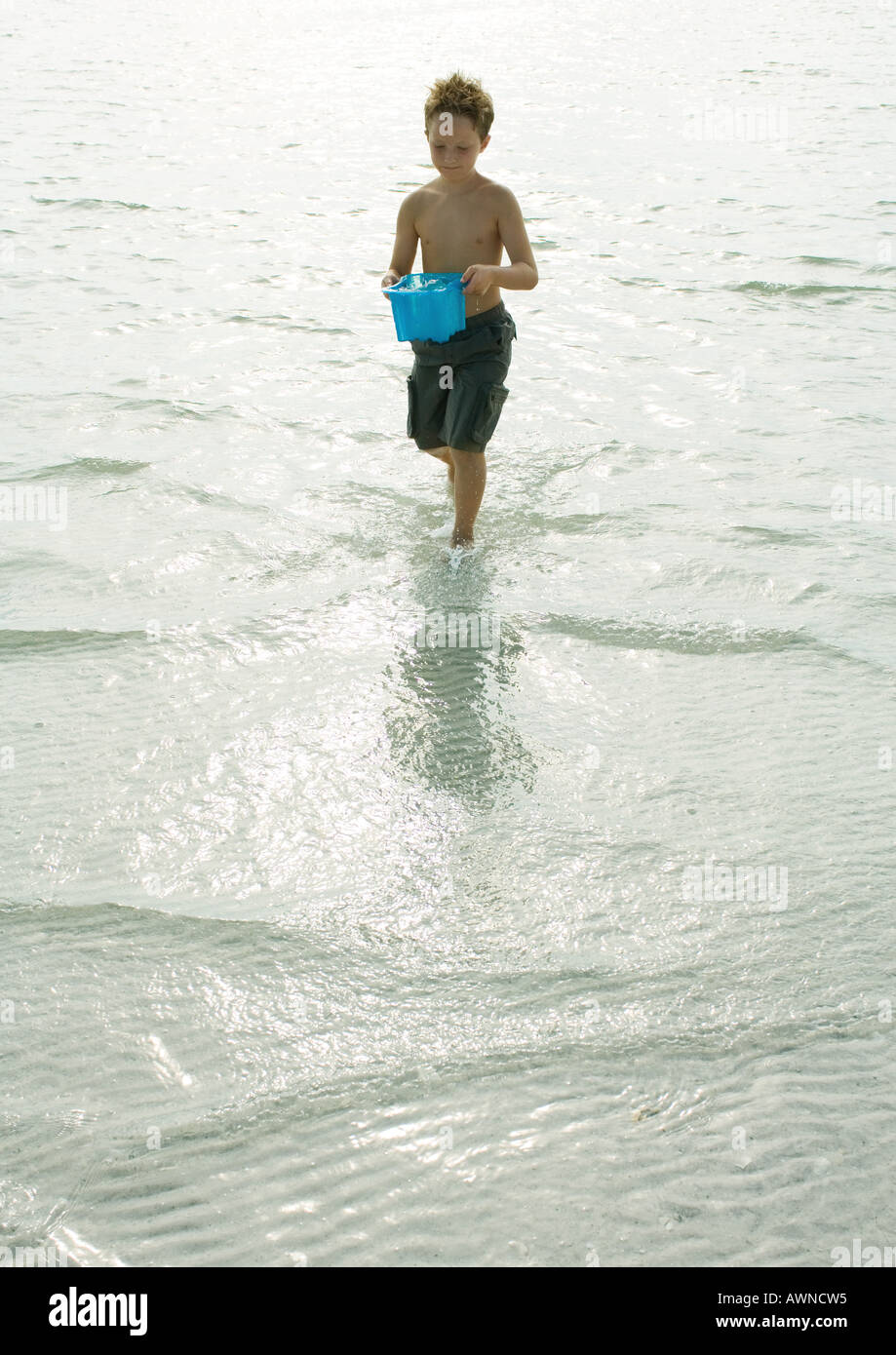 Boy walking through surf with bucket full of water Stock Photo Alamy