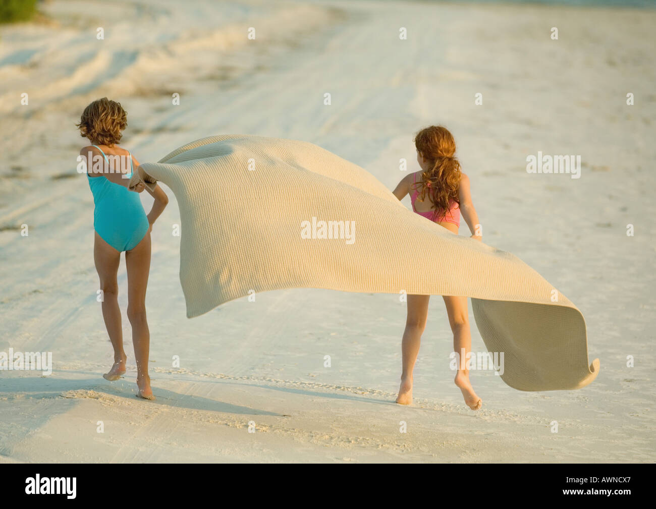 Two Girls Running On Beach Holding Blanket Out In Wind