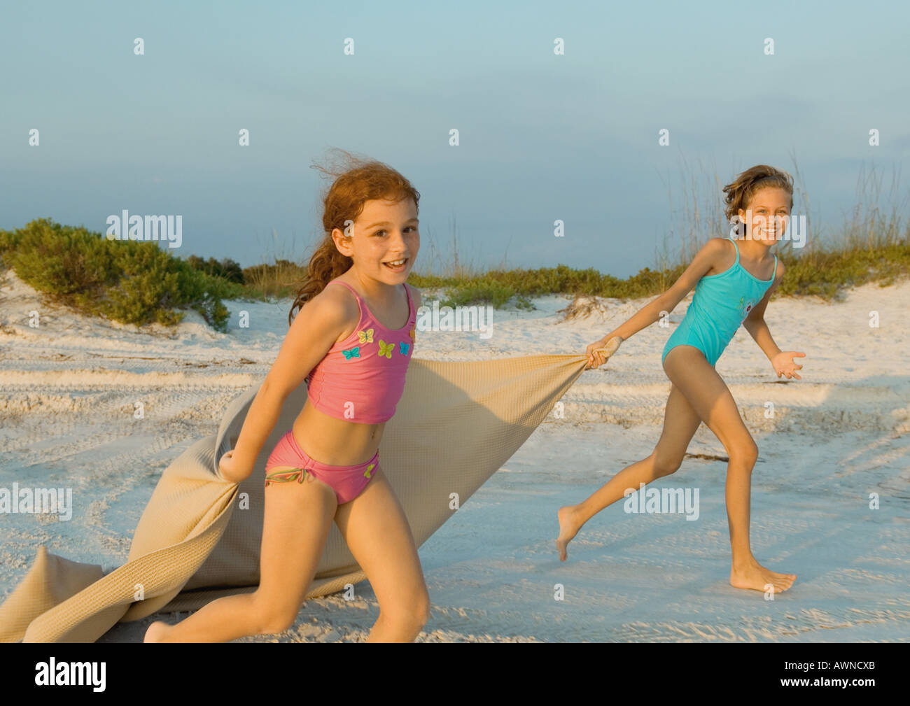 Two Girls Running On Beach Holding Blanket Out In Wind