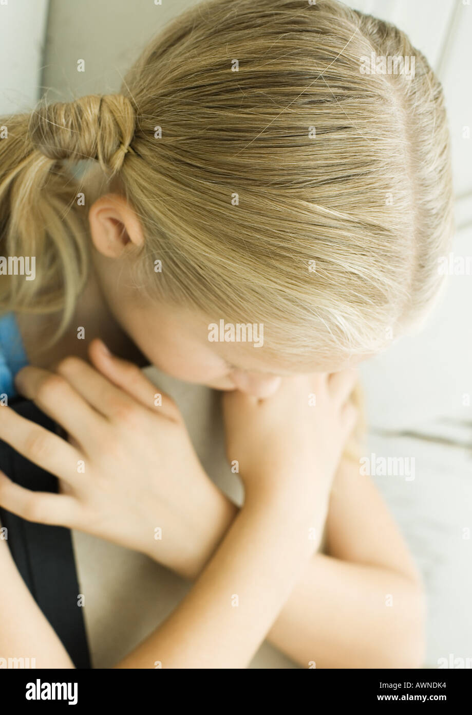 Girl holding book in front of chest, arms crossed and head down Stock