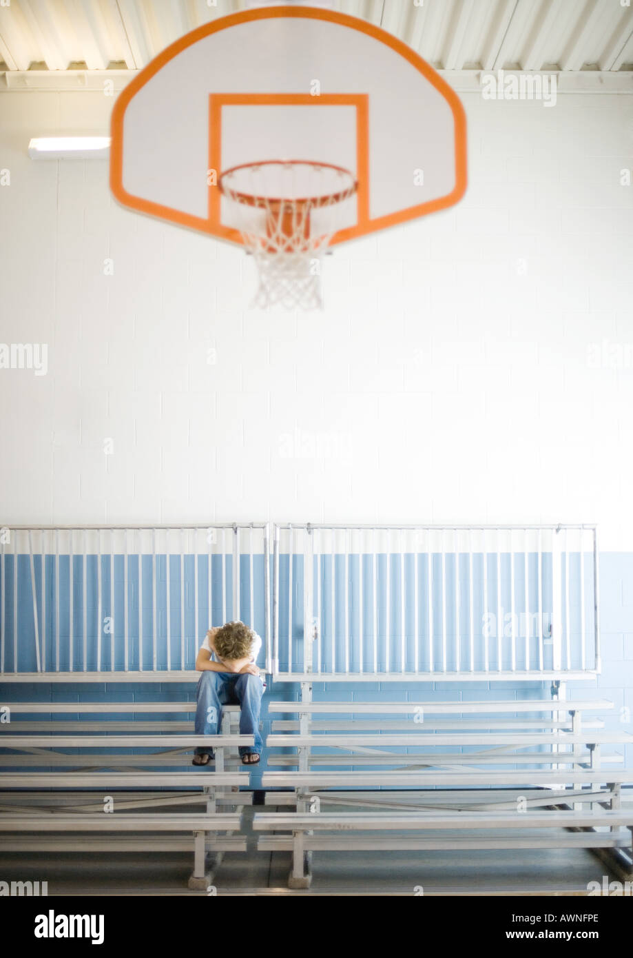 Teenage boy sitting alone with head down in school gym Stock Photo