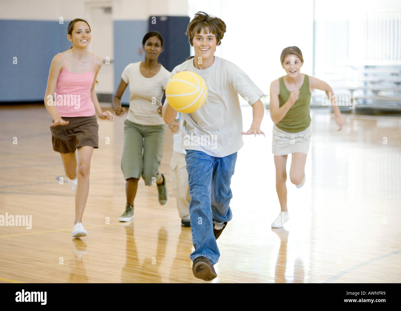 Teenage boy running with basketball in school gym, followed by classmates Stock Photo