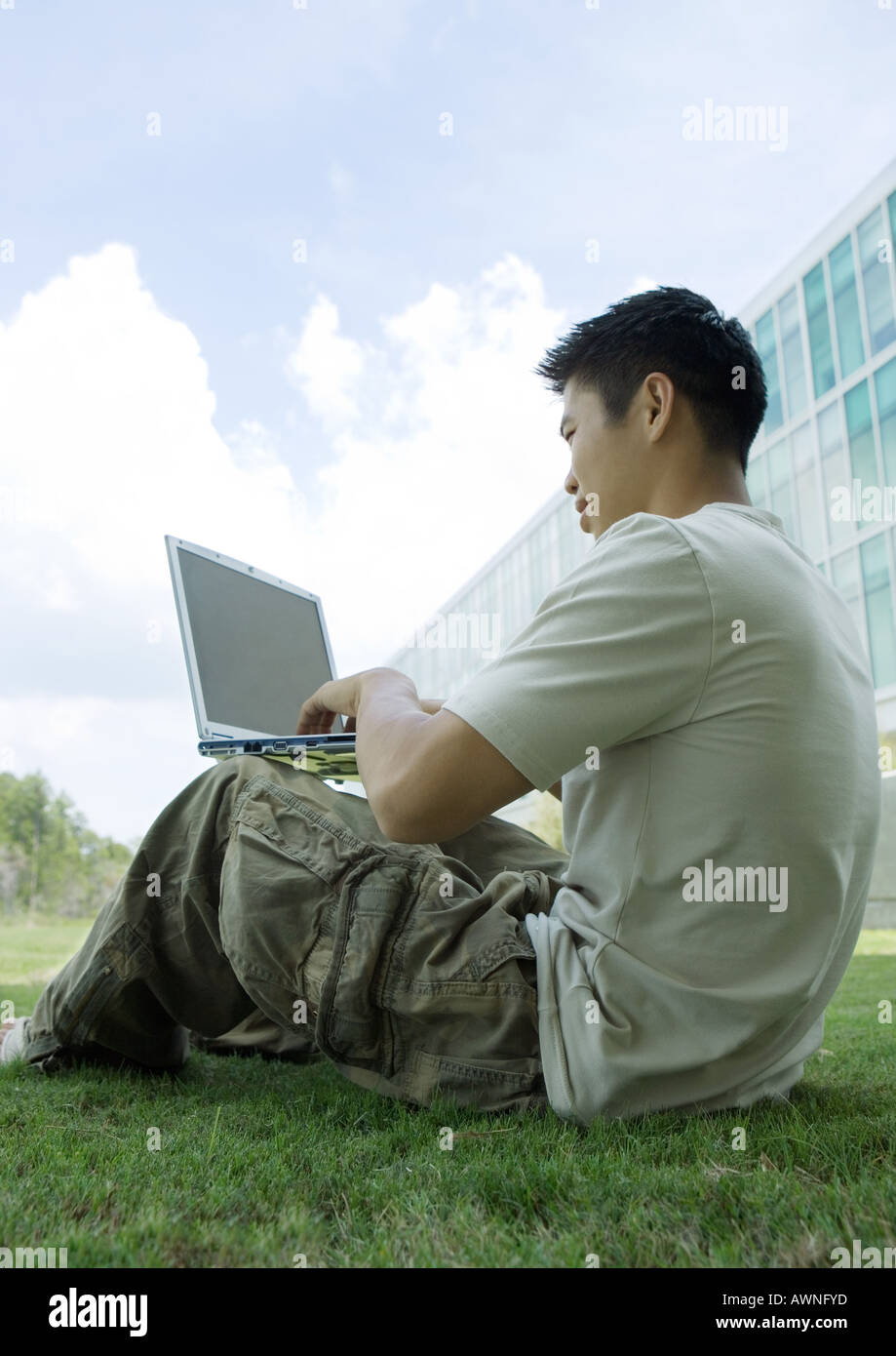 Male college student sitting on grass in campus, using laptop Stock Photo