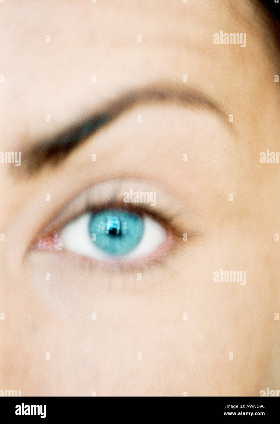 Woman's blue eye and raised eyebrow, looking at camera, close-up, blurred. Stock Photo