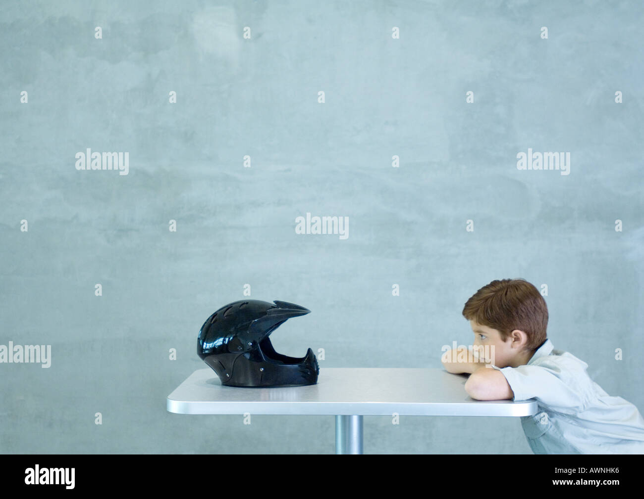 Boy leaning on table, facing helmet Stock Photo