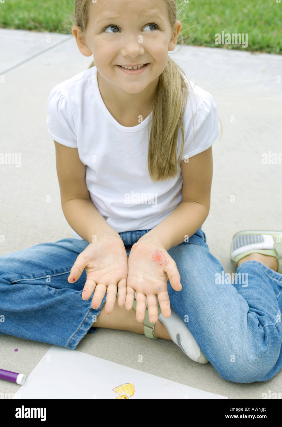 Girl sitting with drawing materials, showing marks on palms Stock Photo