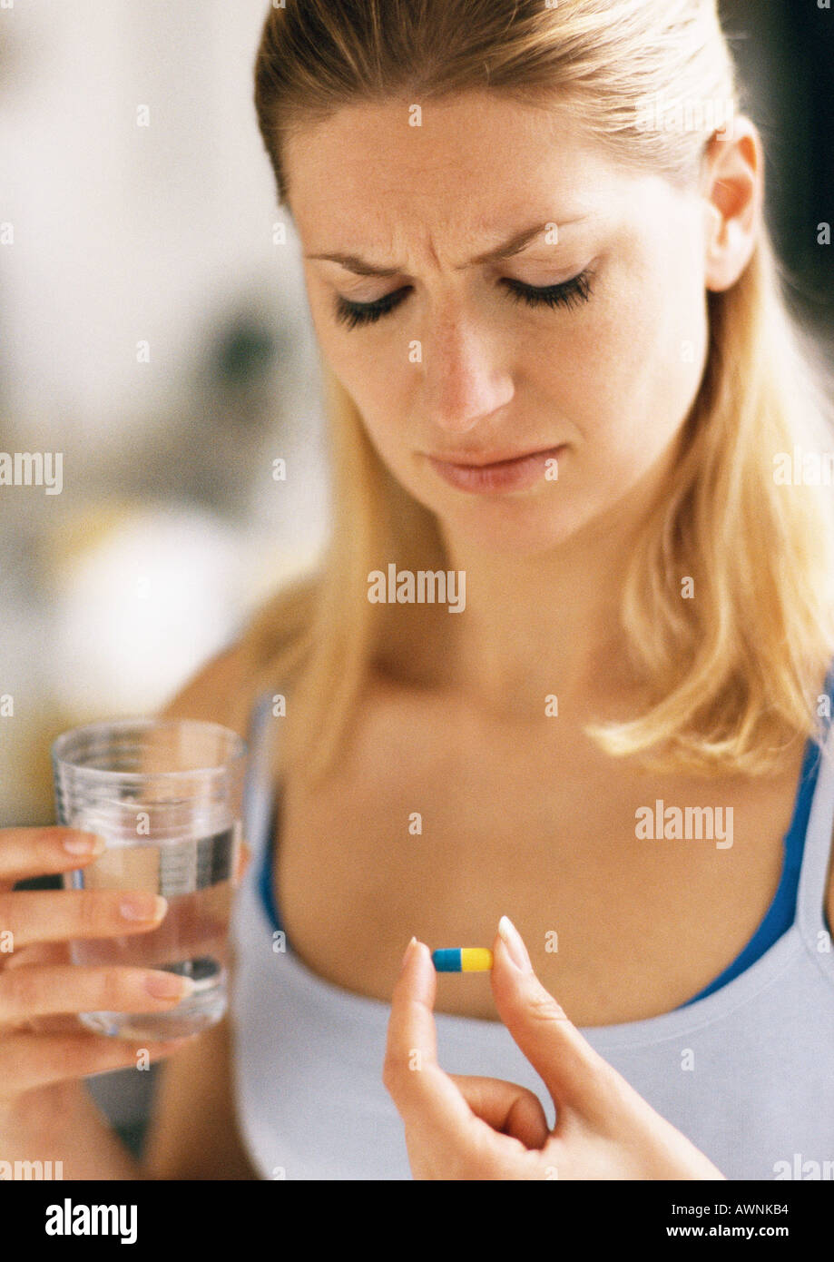Woman holding pill and glass, looking down, head and shoulders, close-up Stock Photo