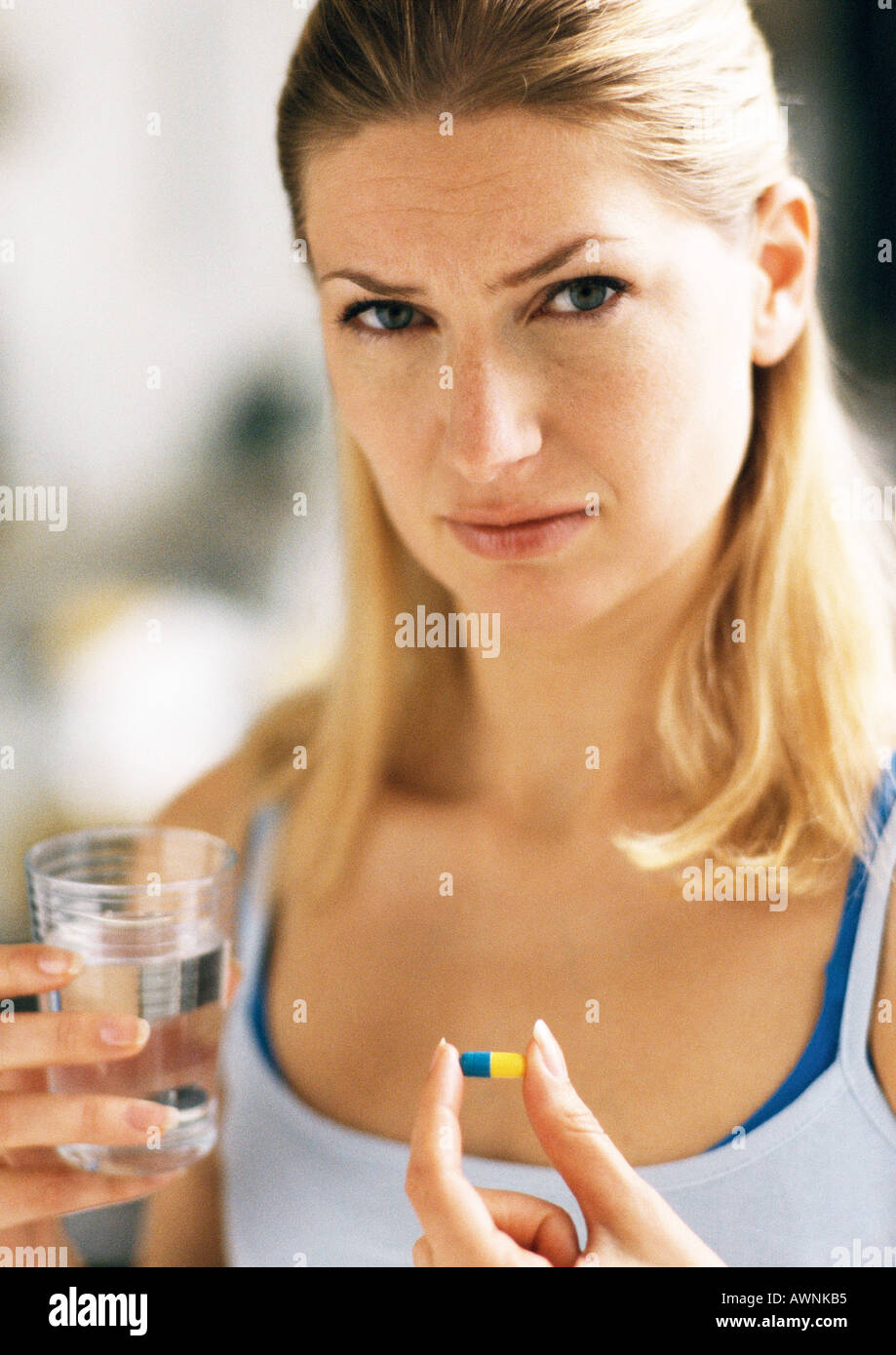 Woman holding pill and glass, looking at camera. Stock Photo