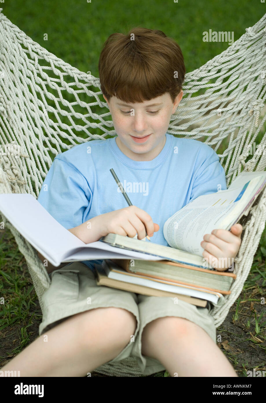 Boy sitting in hammock doing homework Stock Photo