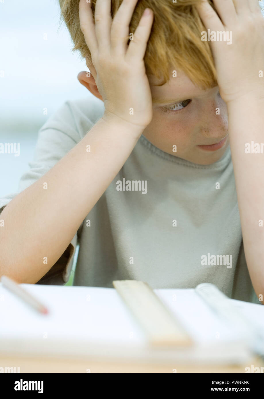 Boy holding head, looking away from homework Stock Photo