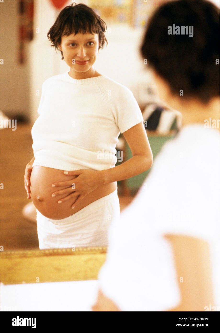 Pregnant woman looking at herself in mirror Stock Photo
