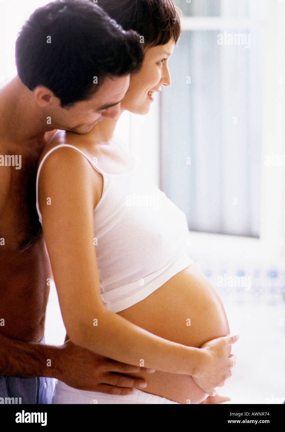 Man holding pregnant woman's waist and looking over her shoulder, side view Stock Photo