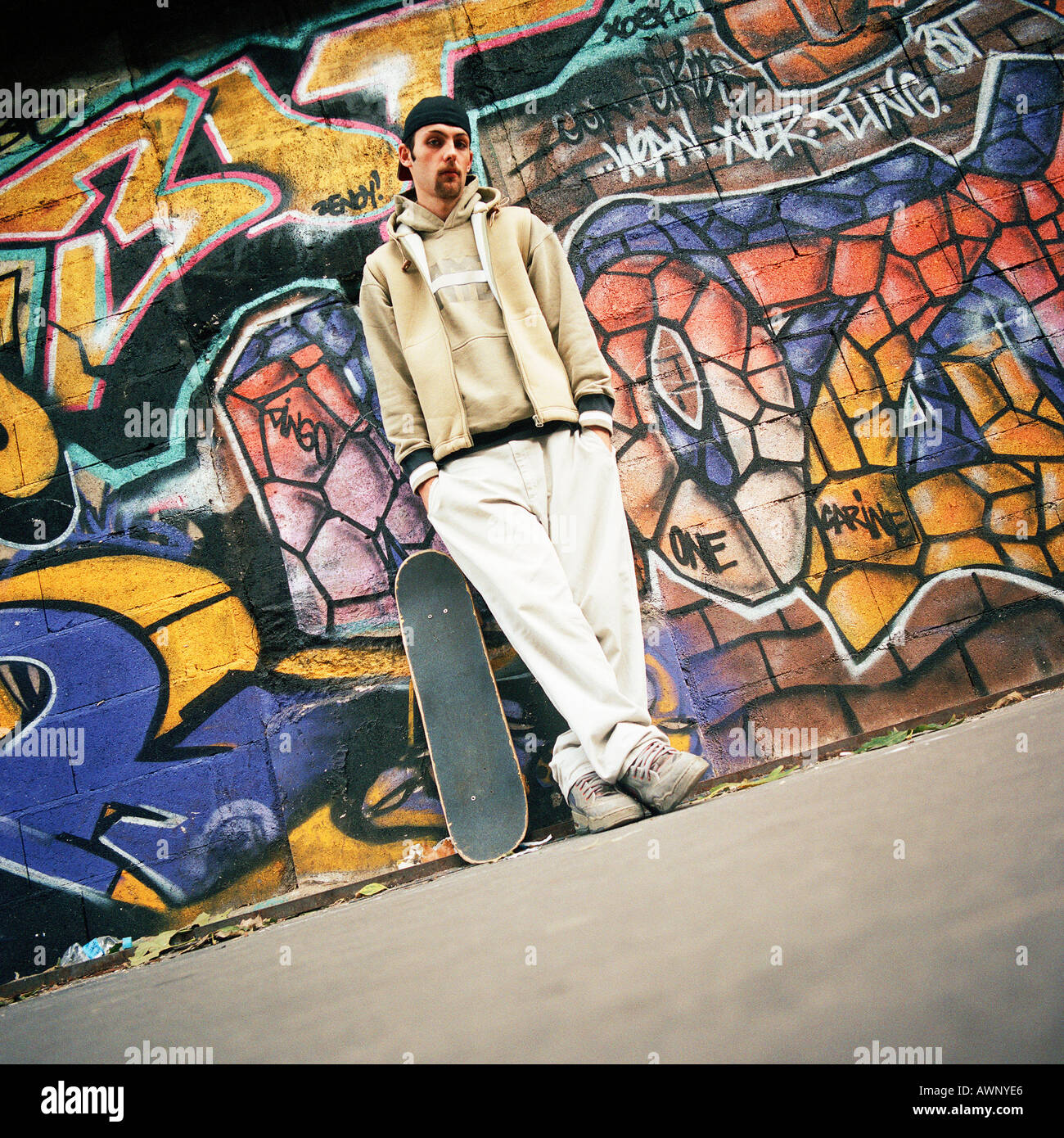Young man with skateboard leaning against graffitied wall, portrait