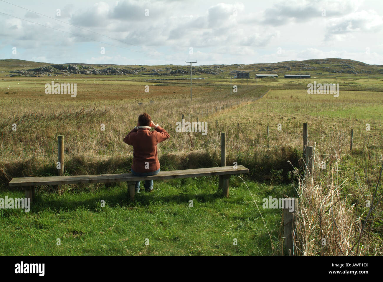 Woman sat watching birds with binoculars near the RSPB information centre at Totronald on the Isle of Coll, Scotland, UK. Stock Photo