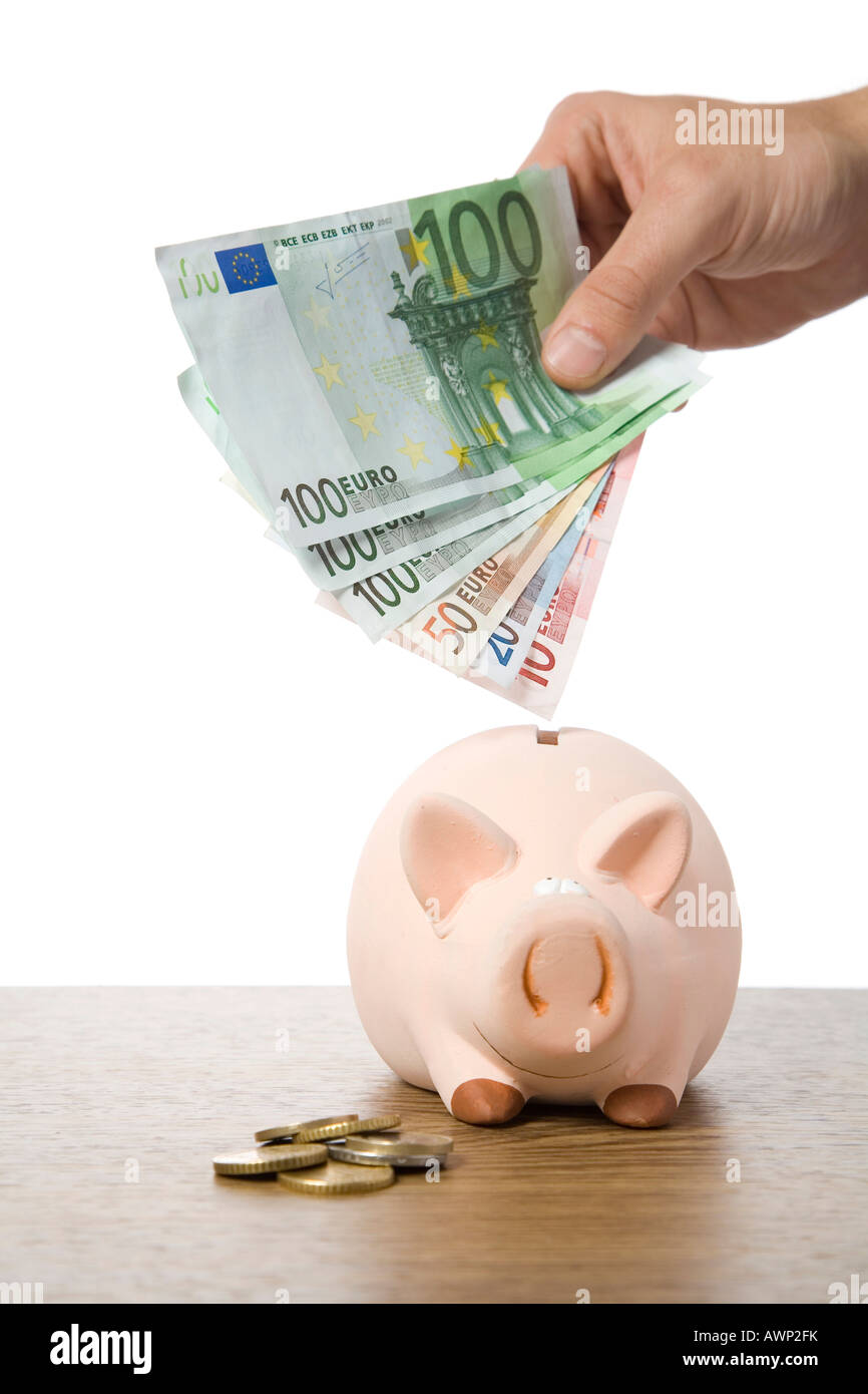 Hand putting money into a piggy bank Stock Photo
