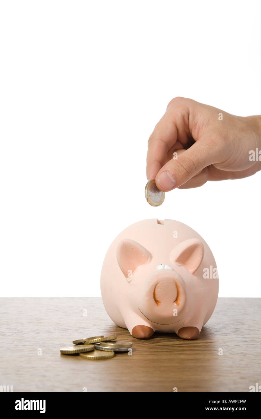 Hand putting a Euro coin into a piggy bank Stock Photo - Alamy