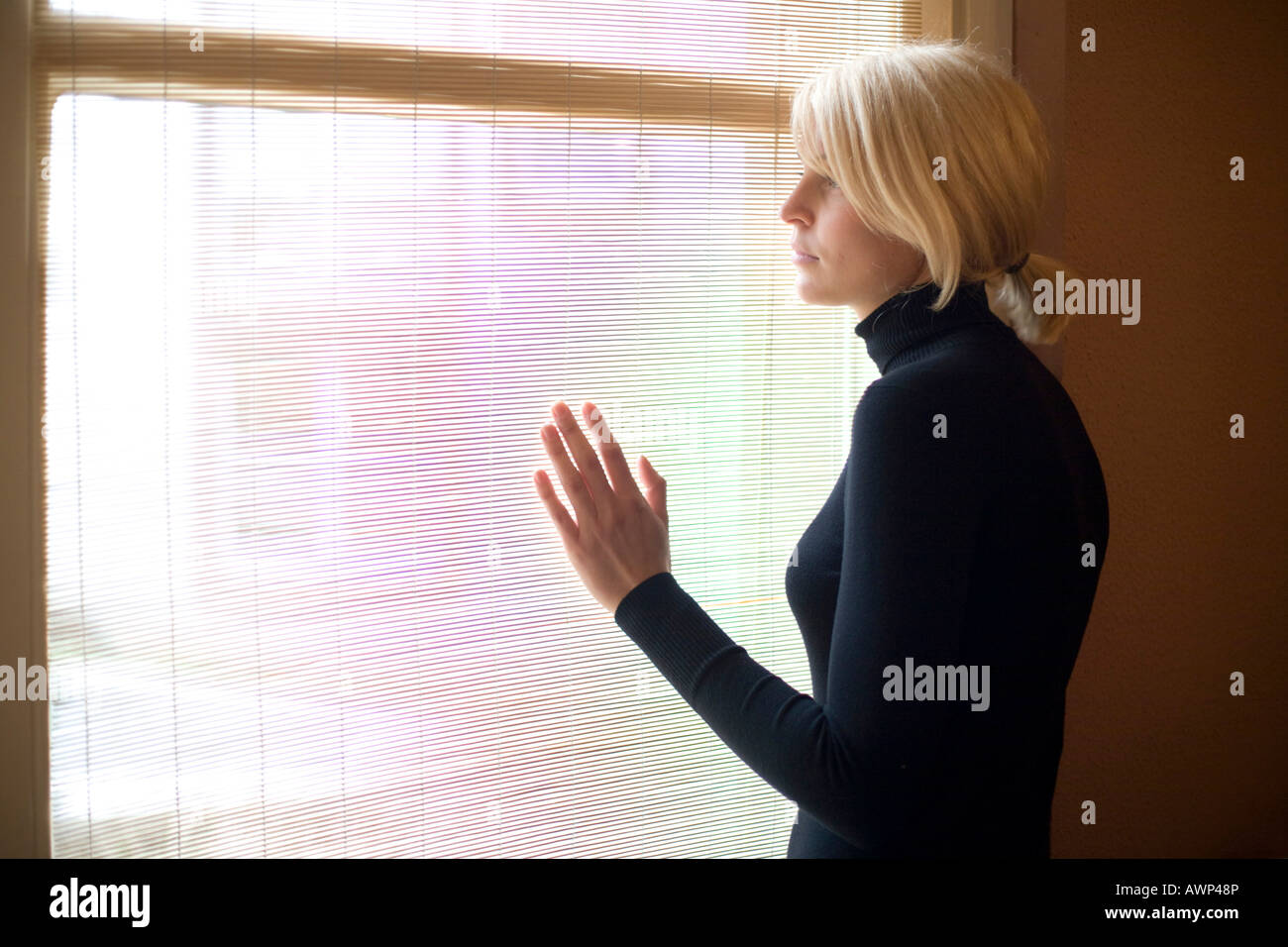 Young blonde woman looking out a window Stock Photo