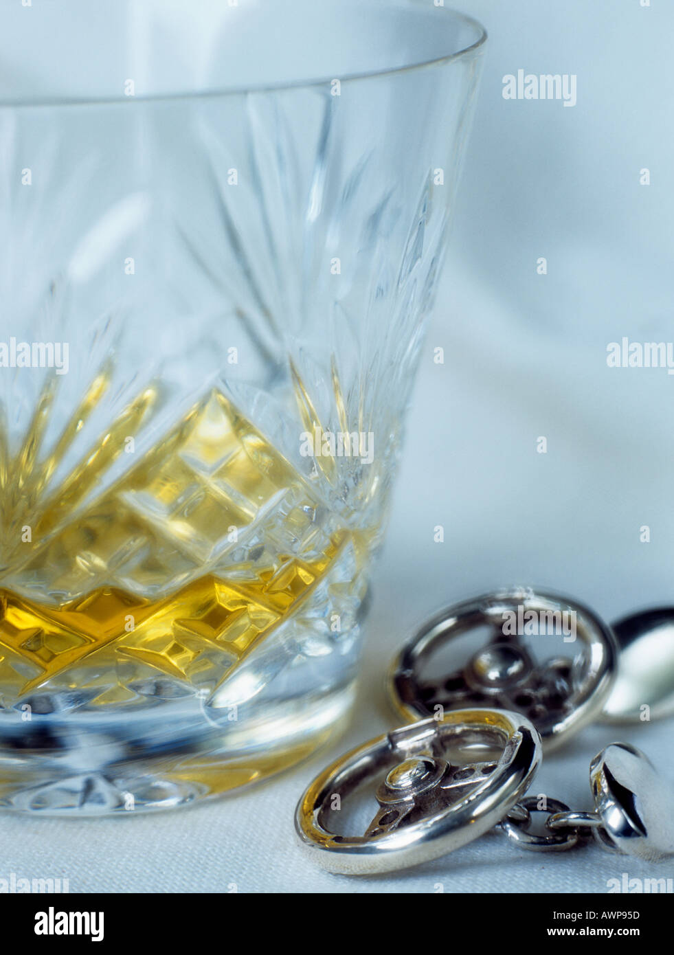 A shot of single malt whiskey in a crystal cut whisky glass tumbler beside men's Steering Wheel cuff links to illustrate don't drink drive concept. UK Stock Photo