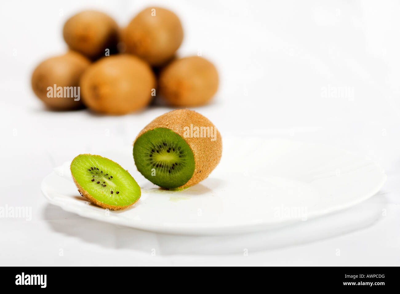 Single kiwi cut open on a plate, more kiwis piled at the back Stock Photo