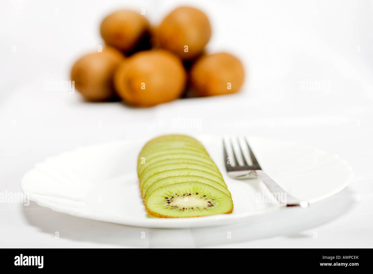 Single sliced kiwi on a plate with fork, more kiwis piled at the back Stock Photo