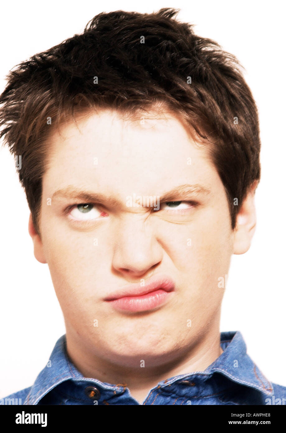 Teenage boy rolling eyes and raising one corner of mouth, head shot, close-up, white background Stock Photo