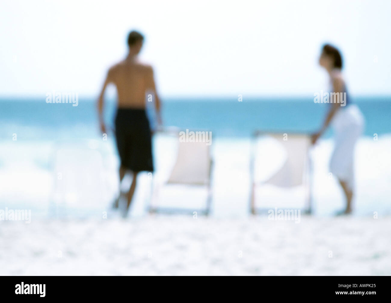 Two adults standing next to chairs on beach, blurred Stock Photo