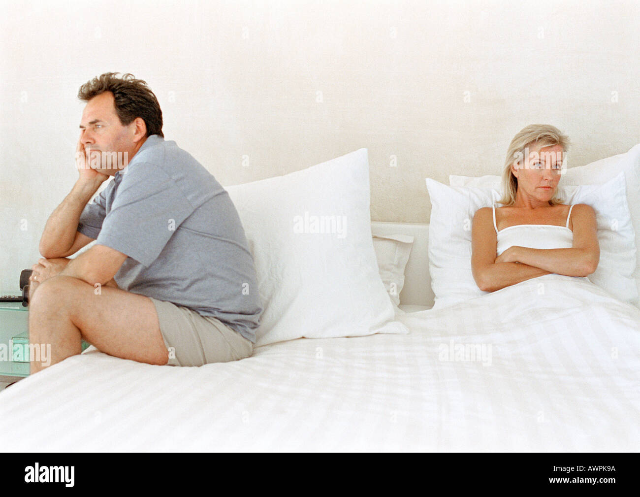Woman in bed with arms crossed, man sitting on side of bed Stock Photo