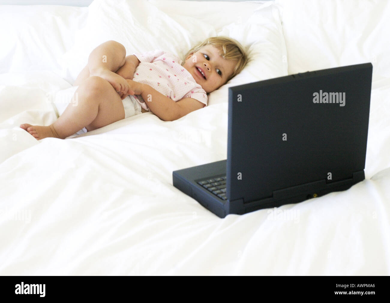 Baby lying on bed, looking at laptop computer Stock Photo - Alamy