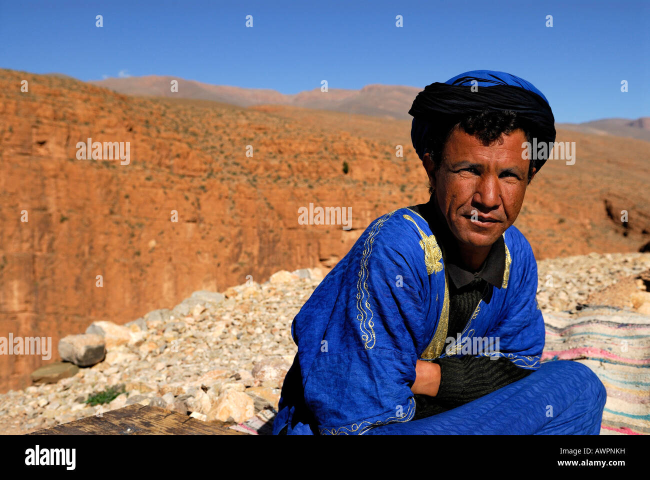 Moroccan dressed in blue sitting in front of red rocks, Dades Gorge, Quarzazate, Morocco, North Africa Stock Photo