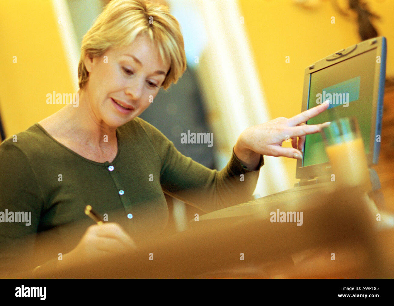 Mature woman using laptop, taking notes Stock Photo