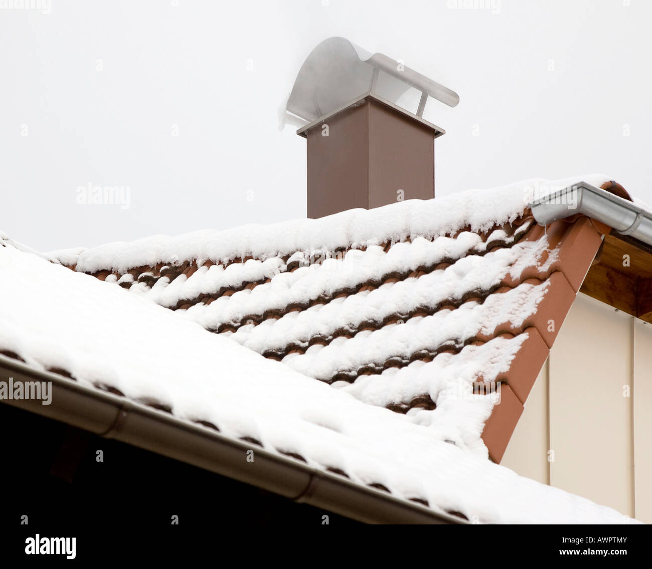 A snow covered roof with a smoking chimney Stock Photo