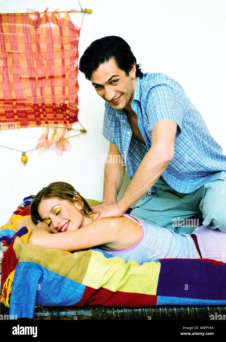 Woman lying on bed smiling, man giving her massage, looking into camera. Stock Photo