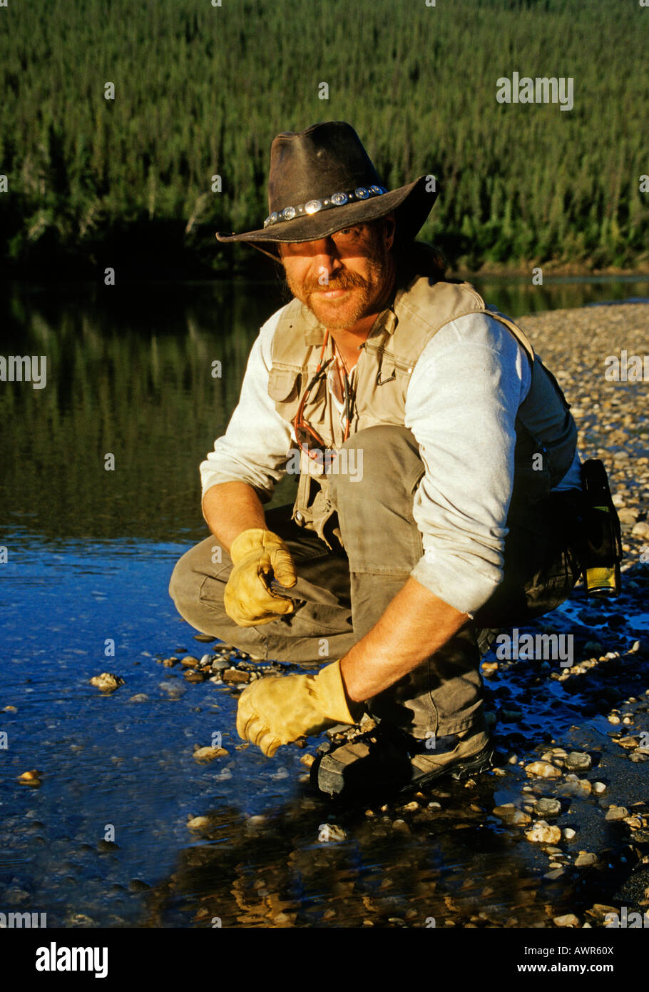 Man crouching at river's edge, Brooks Range, Alaska Stock Photo