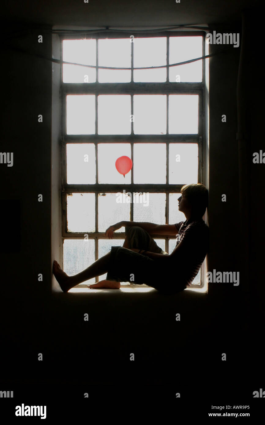 sillhouette of a boy releasing a ballon in a window Stock Photo