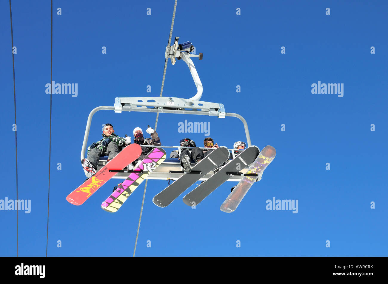 A group of snowboarders sitting on a ski lift against a blue sky ...