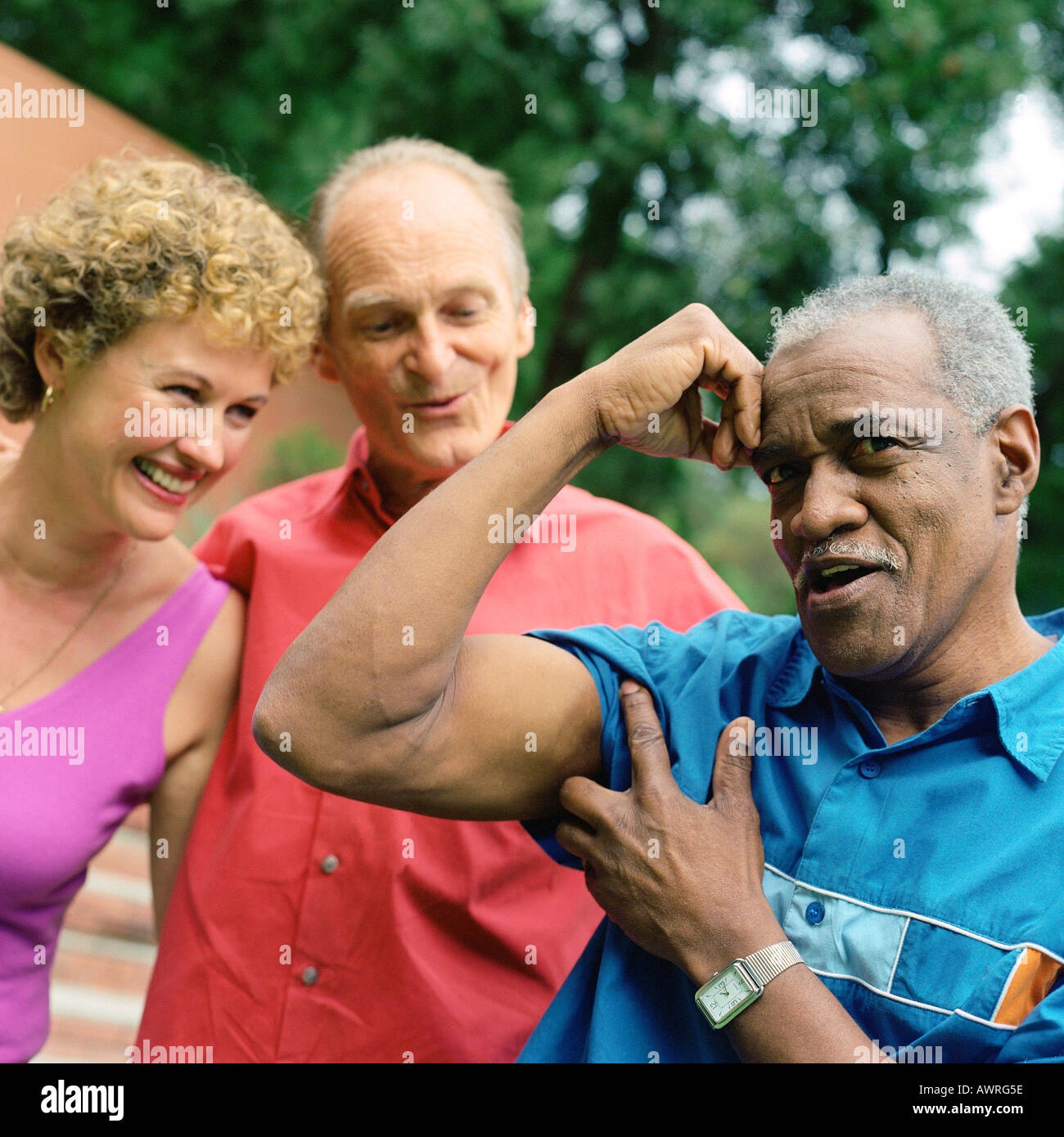 Three people standing outside, man flexing arm muscles Stock Photo