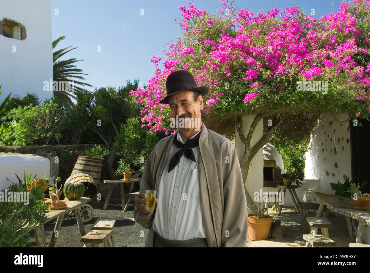Lanzarote Winemaker with white Malvasia wine, outside sunny wine tasting bodega with typical Bougainville & Palm trees, Lanzarote Canary Islands Spain Stock Photo