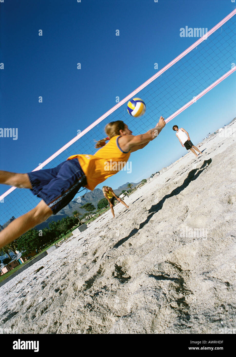 Three young people playing beach volleyball, one midair Stock Photo