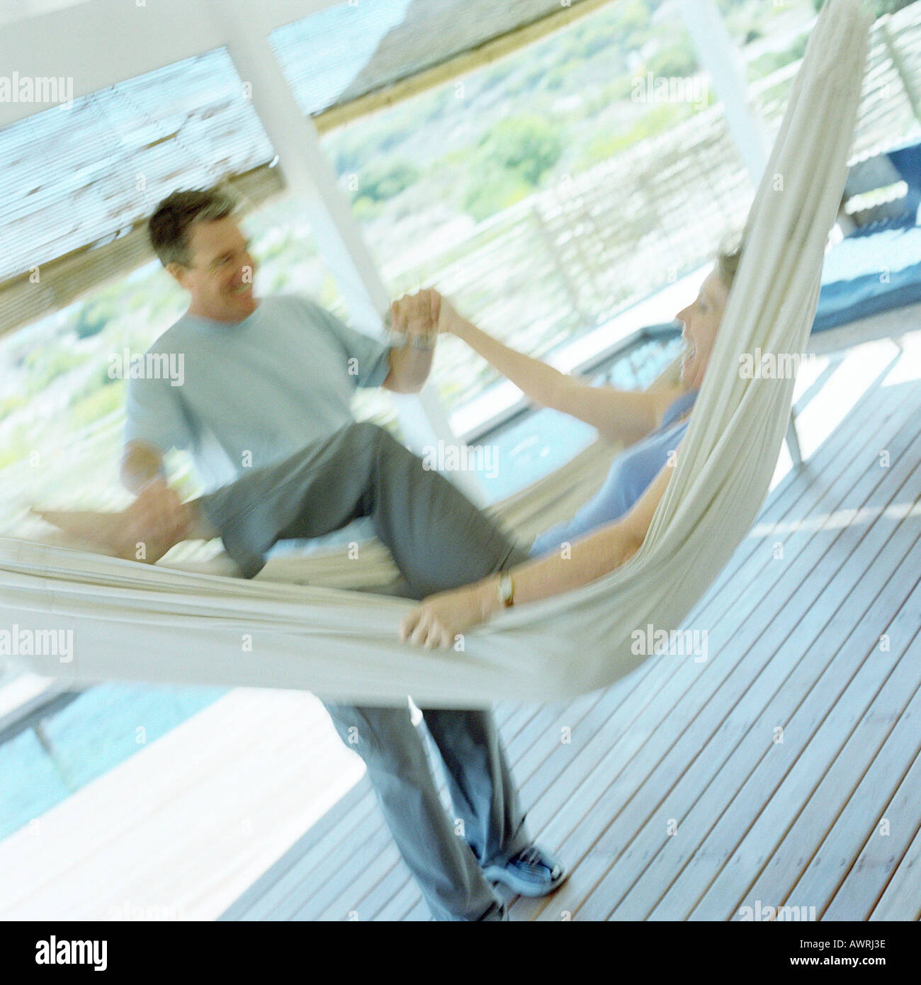 Mature woman laughing in hammock, mature man grabbing her leg and arm, blurred Stock Photo