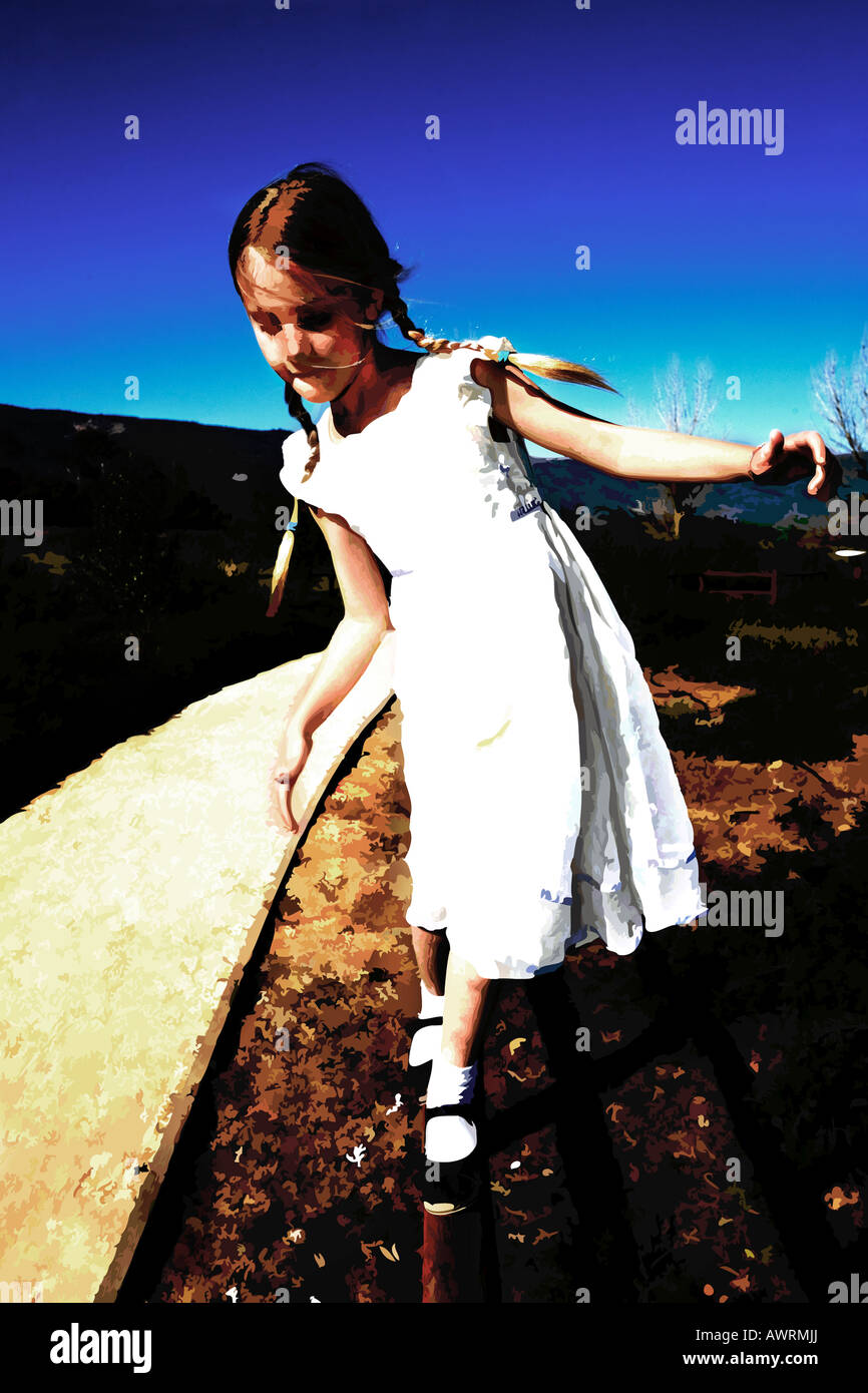 A young girl balances on a fence in a white dress and mary jane shoes. Stock Photo