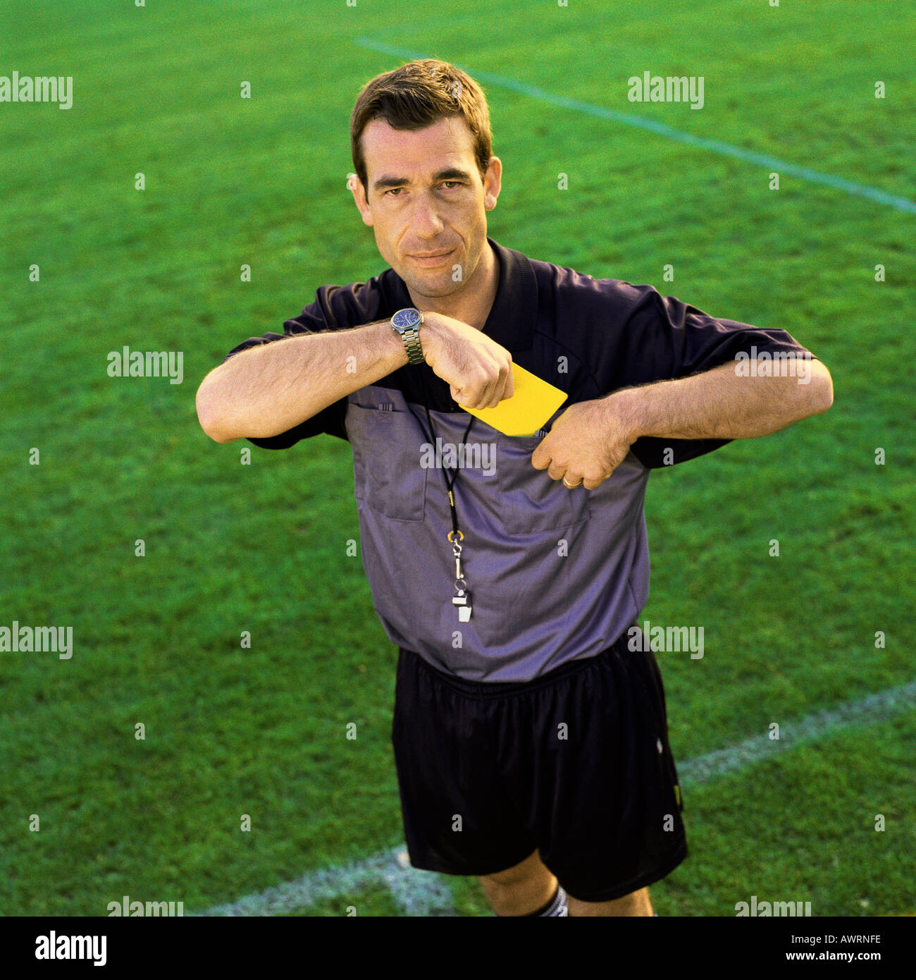 Referee pulling out yellow card, looking into camera. Stock Photo