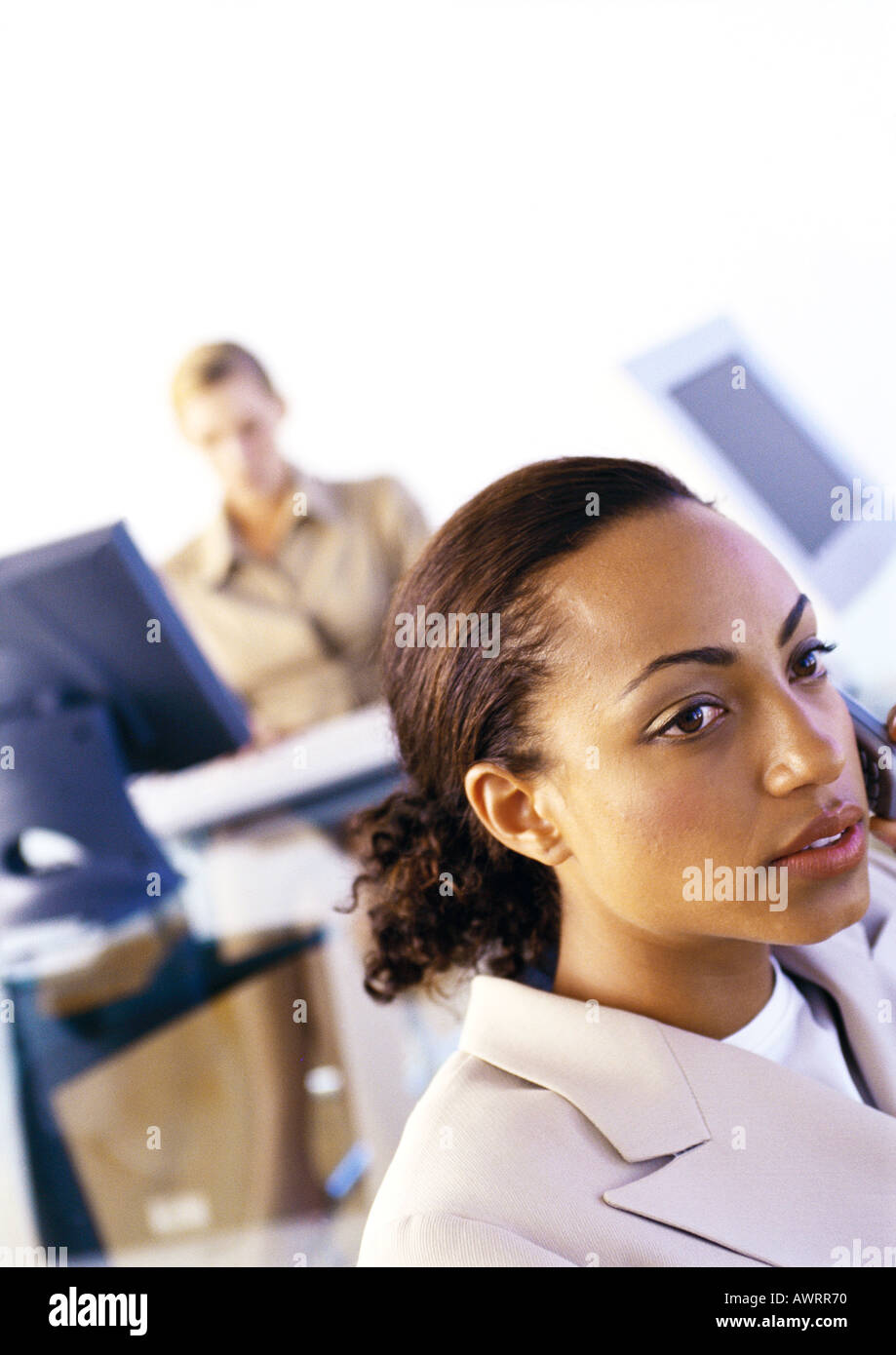 Businesswomen in office, one using cell phone, second using computer Stock Photo