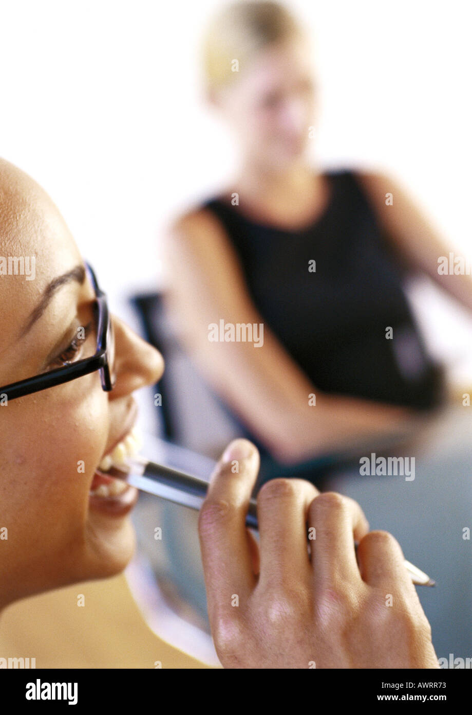 Two businesswoman, one holding pen near mouth, close-up Stock Photo