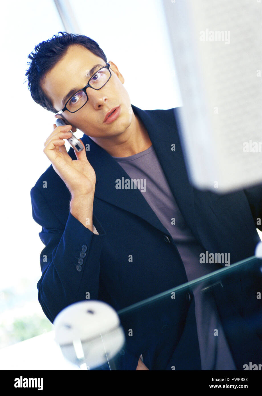 Businessman sitting at computer, using cell phone Stock Photo