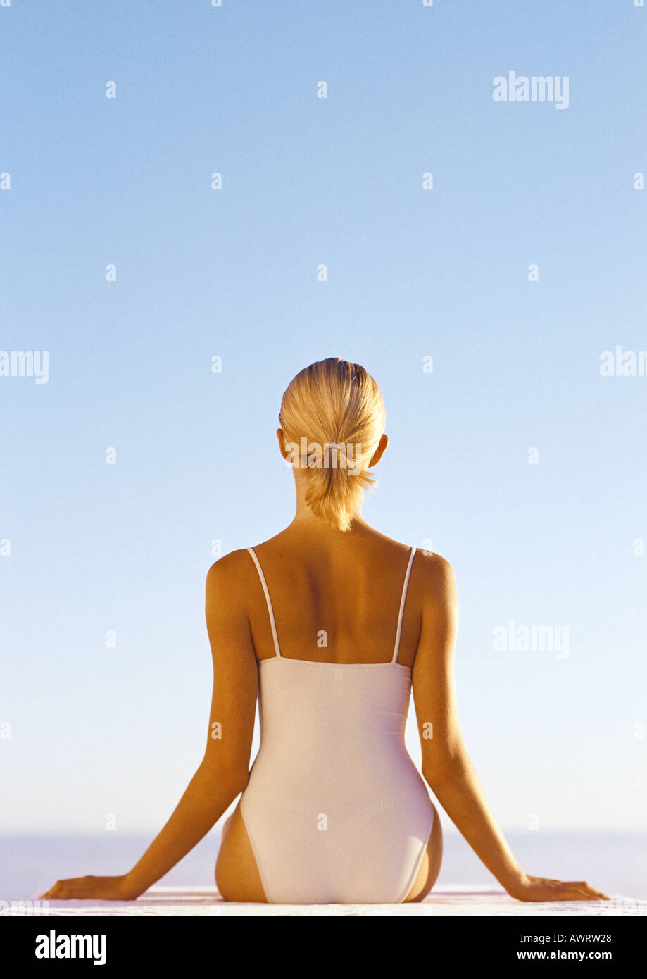 Woman in one-piece bathing suit, hands out to the side, waist up, rear view, blue sky in background Stock Photo
