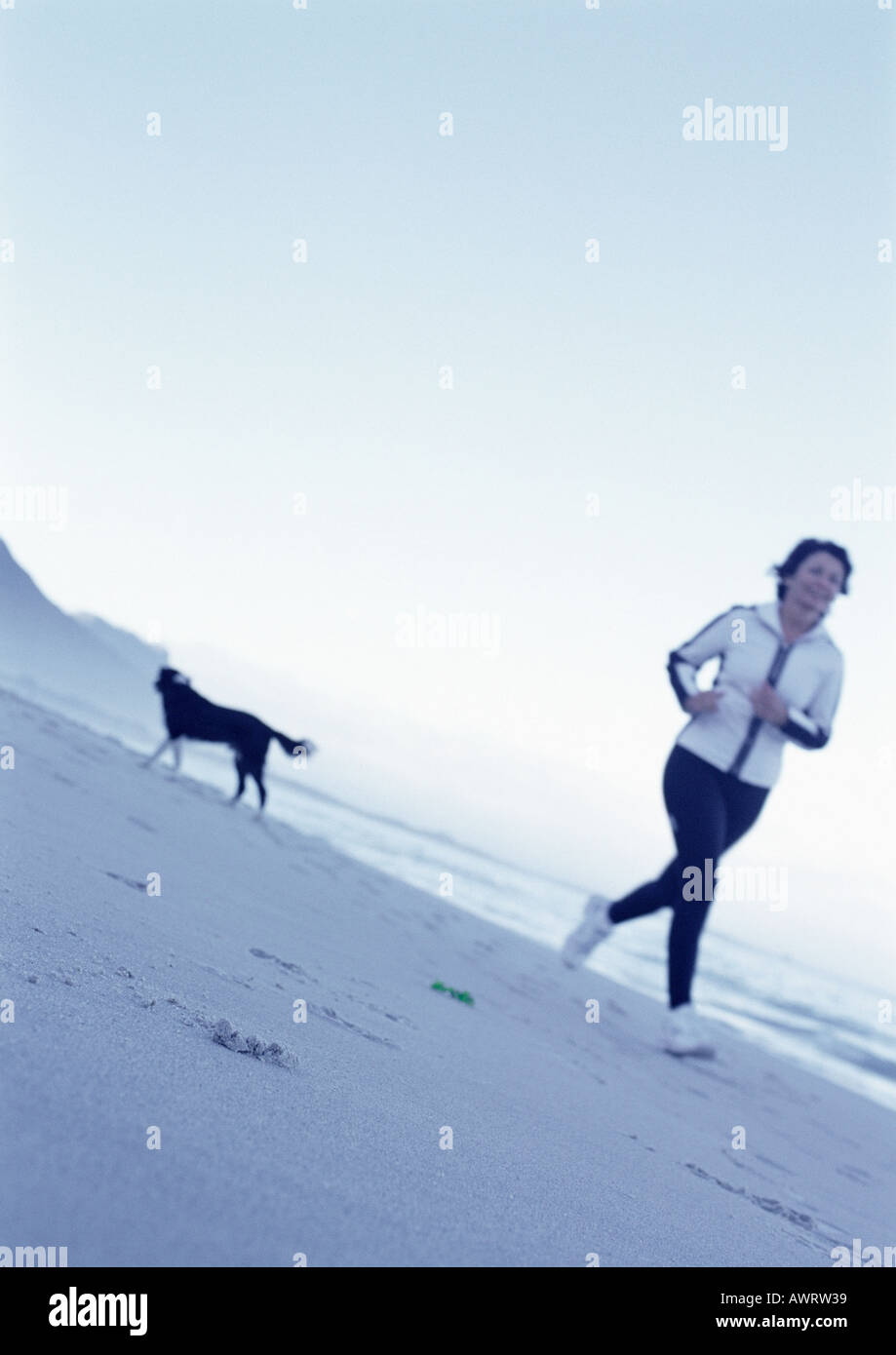 Mature woman running on beach, dog in background Stock Photo