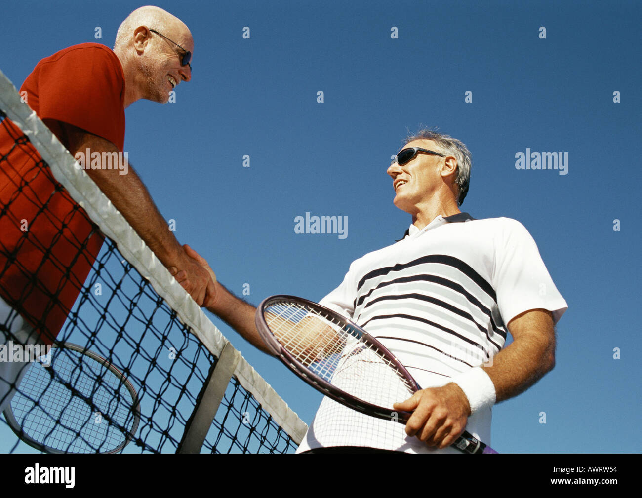 Two mature men shaking hands over tennis net, low angle view Stock Photo