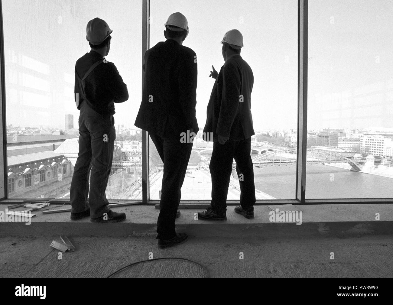 Three men wearing hard hats, looking out of window, rear view, b&w Stock Photo