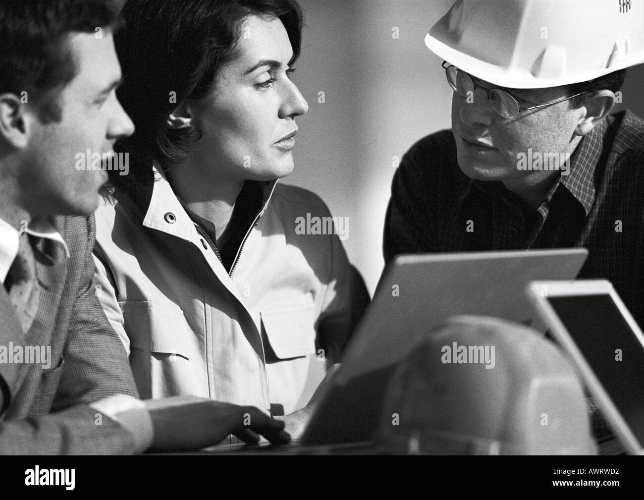 Three people with laptop computer, one with hard hat, head and shoulders, b&w Stock Photo